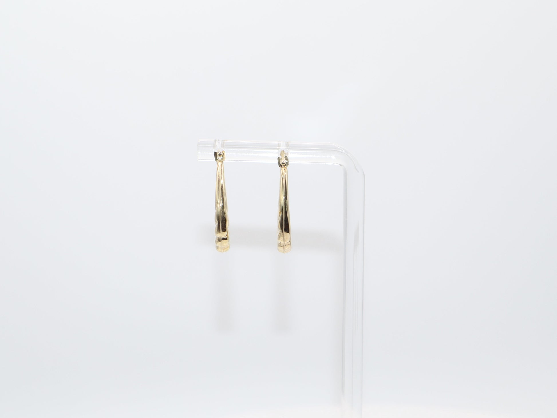 Gold hoop earrings on a clear stand against a white background